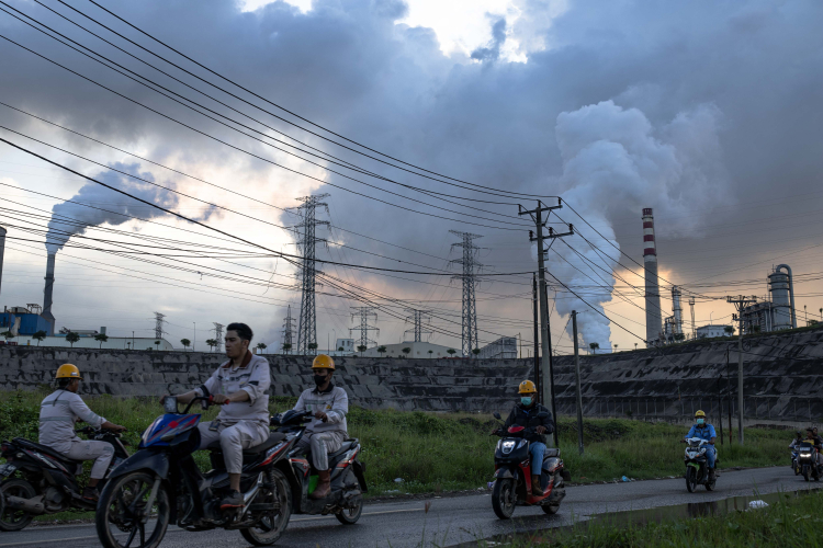 Workers using a motorcycle near the belching chimneys of Indonesia Morowali Industrial Park (IMIP), a nickel processing complex in Morowali, Central Sulawesi, Indonesia on June 12, 2024.